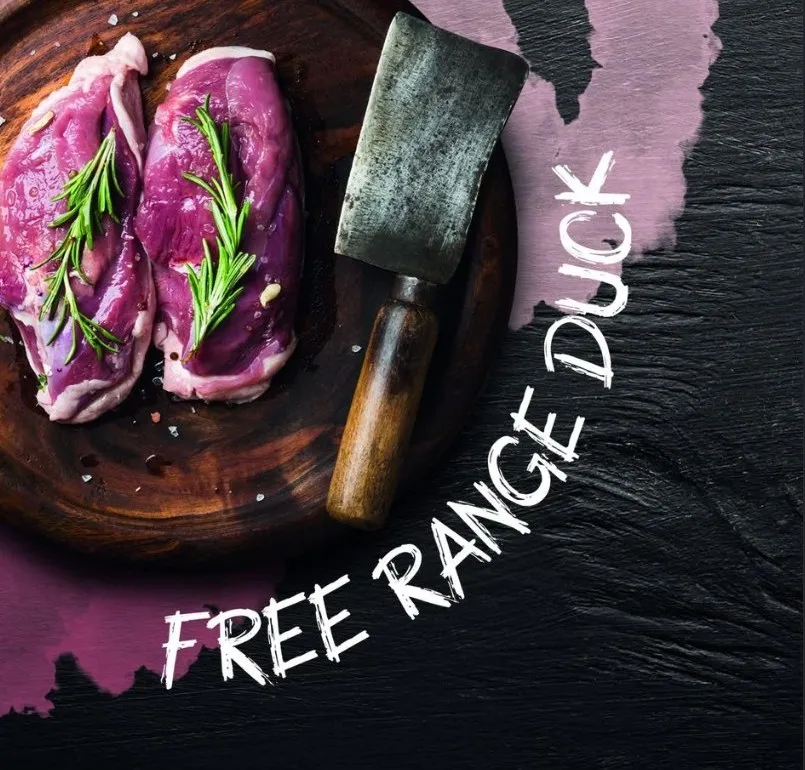 A branded promotional graphic for free-range duck — hand-lettered type and brand colours laid over a photograph of two duck breasts on a wooden board with a cleaver