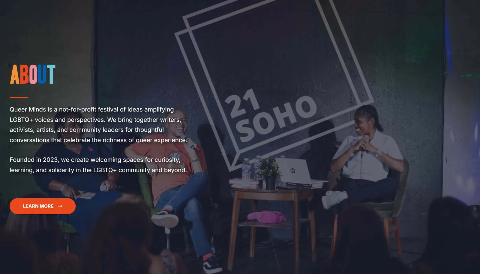 The About section on queerminds.co.uk, its heading set with every letter in a different colour from the festival palette, over a darkened photo of a panel on stage at 21Soho, with two paragraphs and a Learn more button